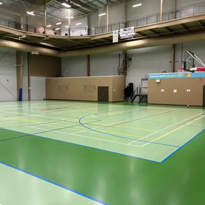 Indoor gym with green courts, basketball hoops, overhead walkway, and scoreboard.