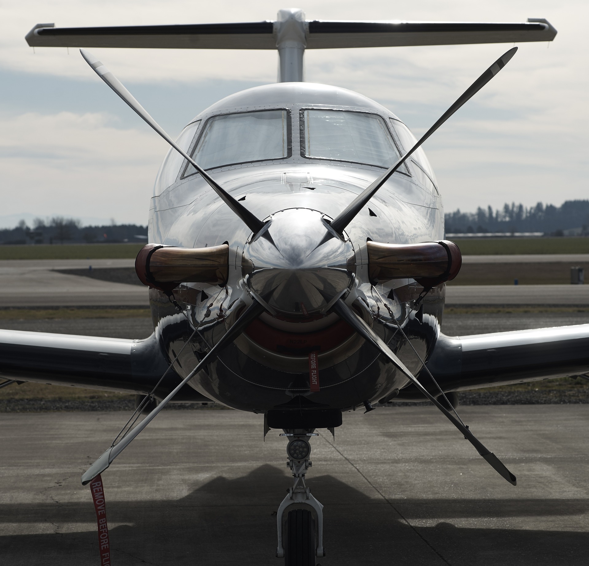 Front view of a polished aircraft with spinning propellers, set against a cloudy sky.