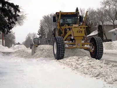 A snowplow clears a snow-covered street in a residential area during winter.