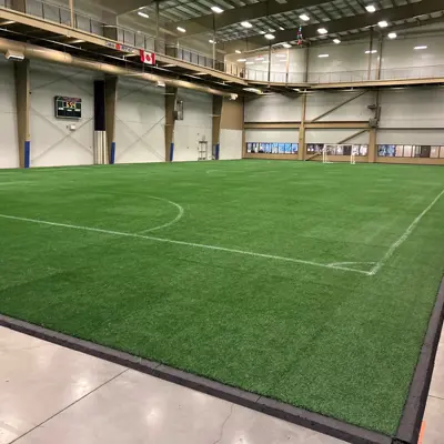 Indoor artificial turf field inside a large gymnasium with overhead lights.