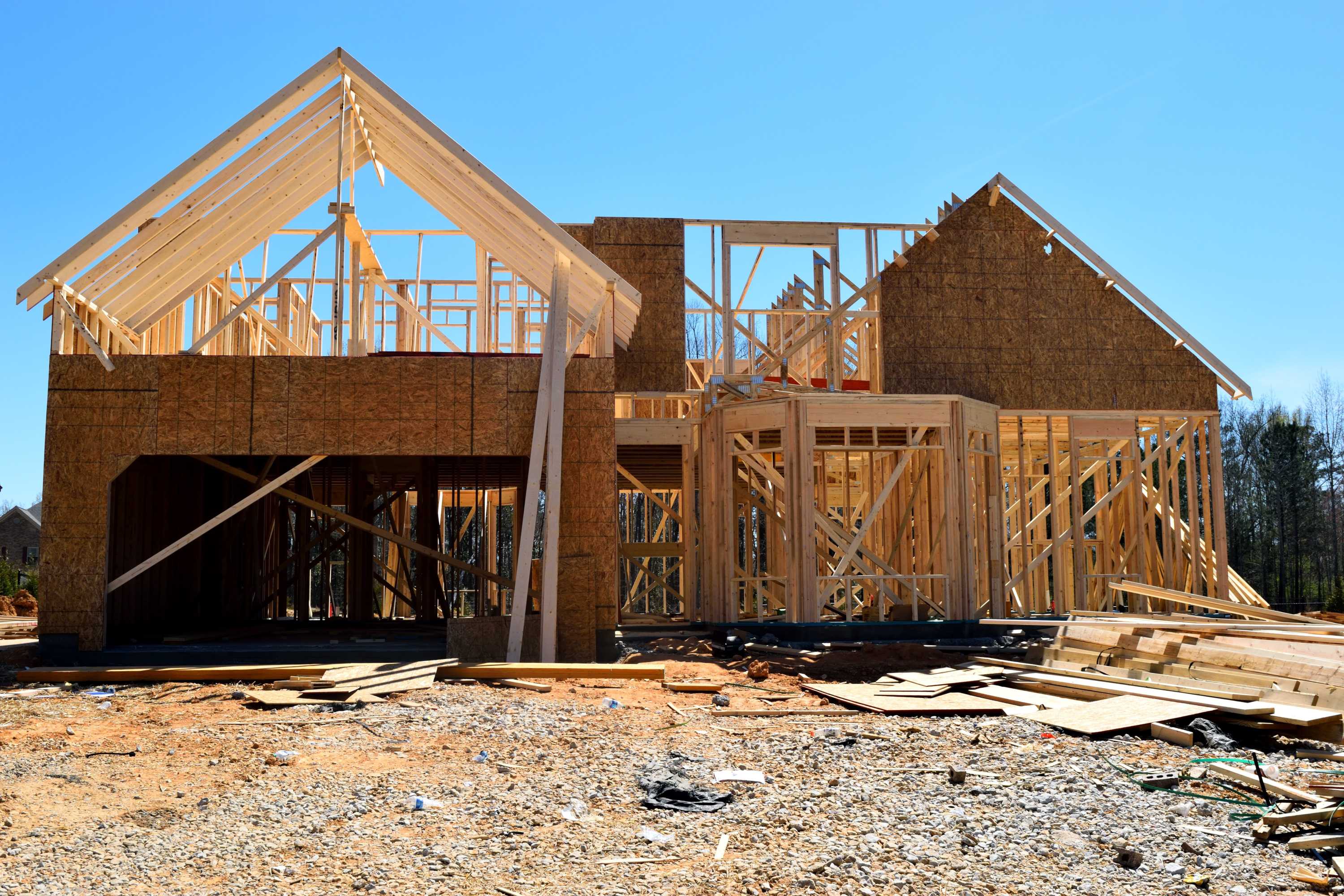 A partially built wooden house with visible framing and construction materials on a sunny site.