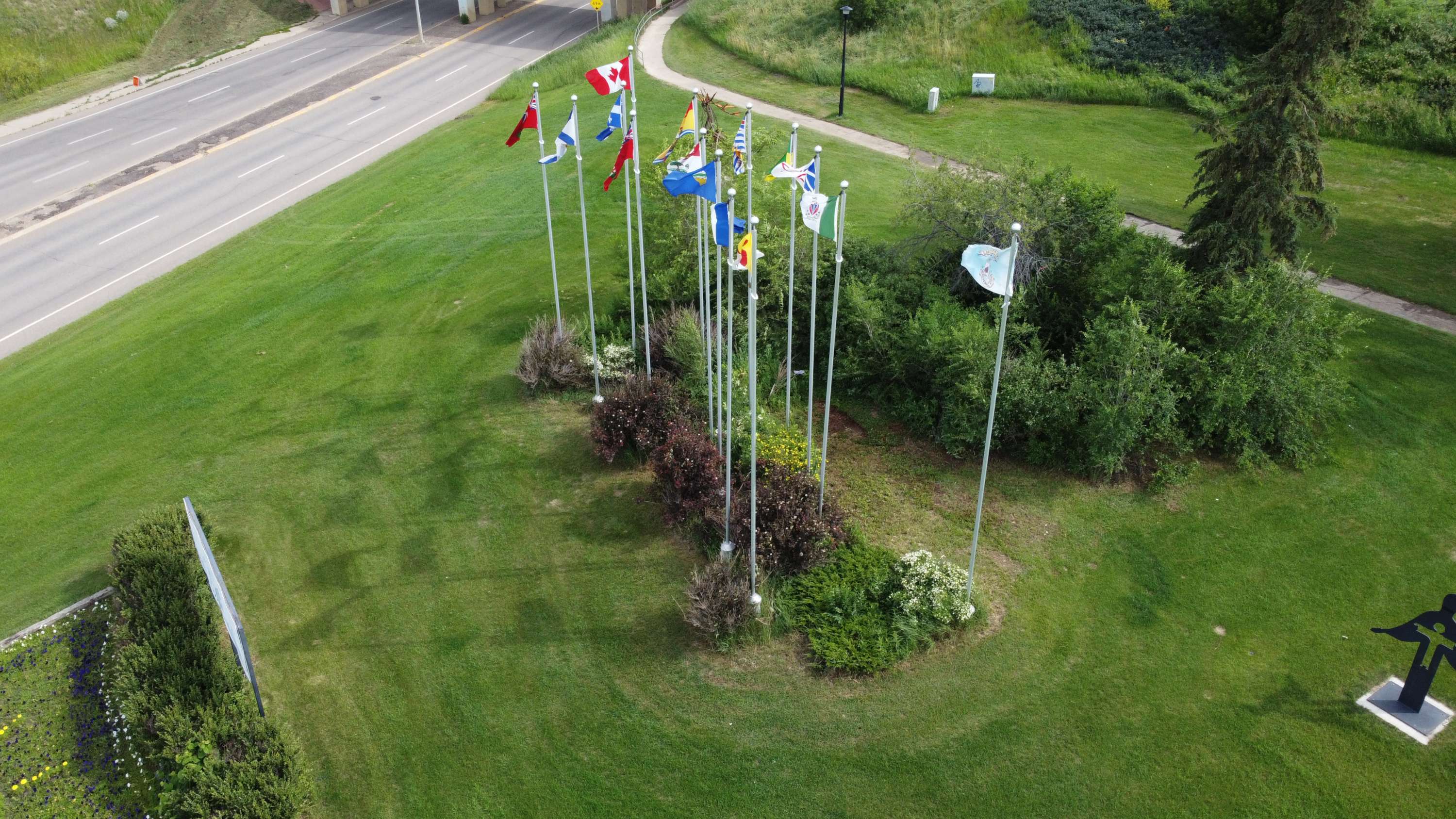 Aerial view of flagpoles displaying Provincial, Canadian, and City flags in a green landscape.