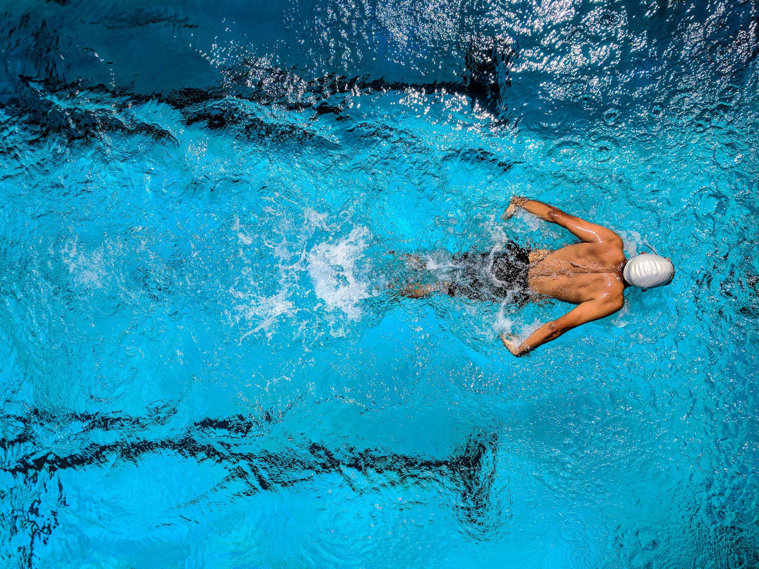 A swimmer gliding through clear blue water, creating ripples and bubbles around them.