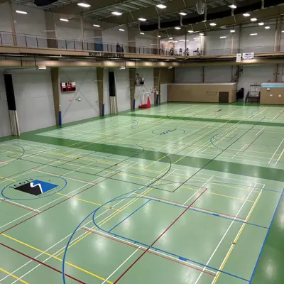 Empty indoor sports hall with green marked courts, nets, and overhead lighting.