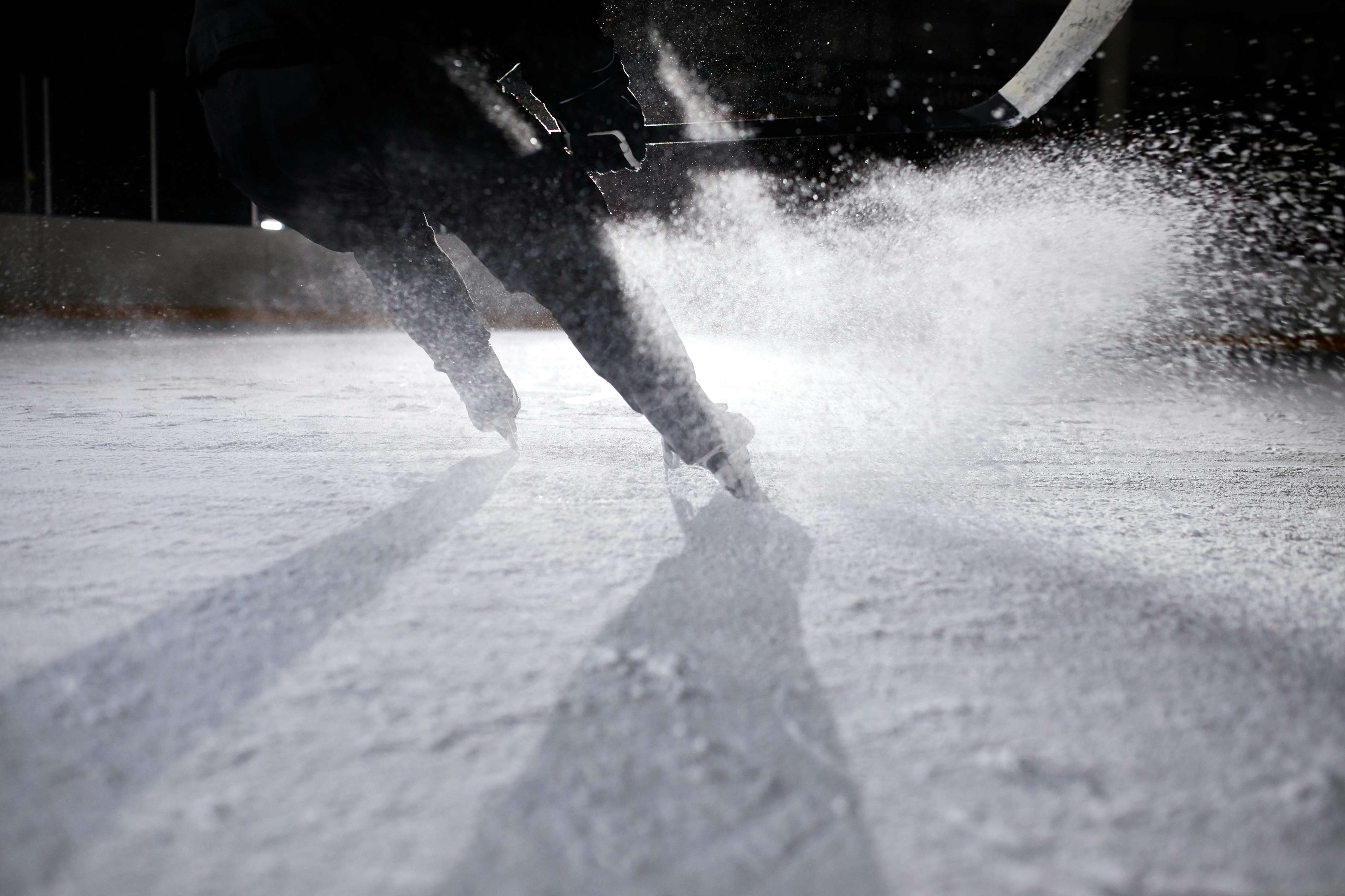 Skater gliding on ice, leaving a trail of snow and shadows in a rink during nighttime.
