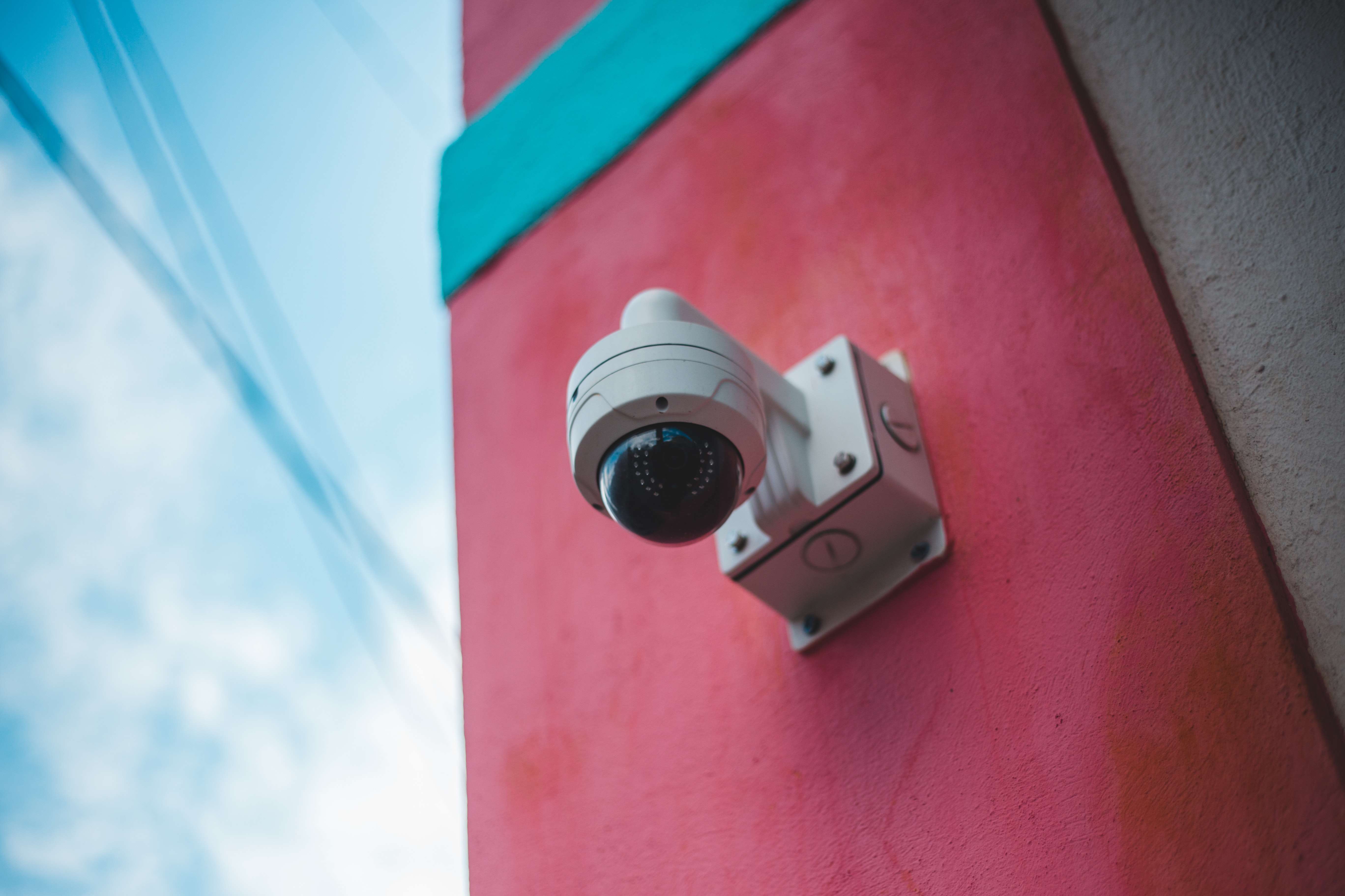 A security camera on a brightly coloured exterior wall.