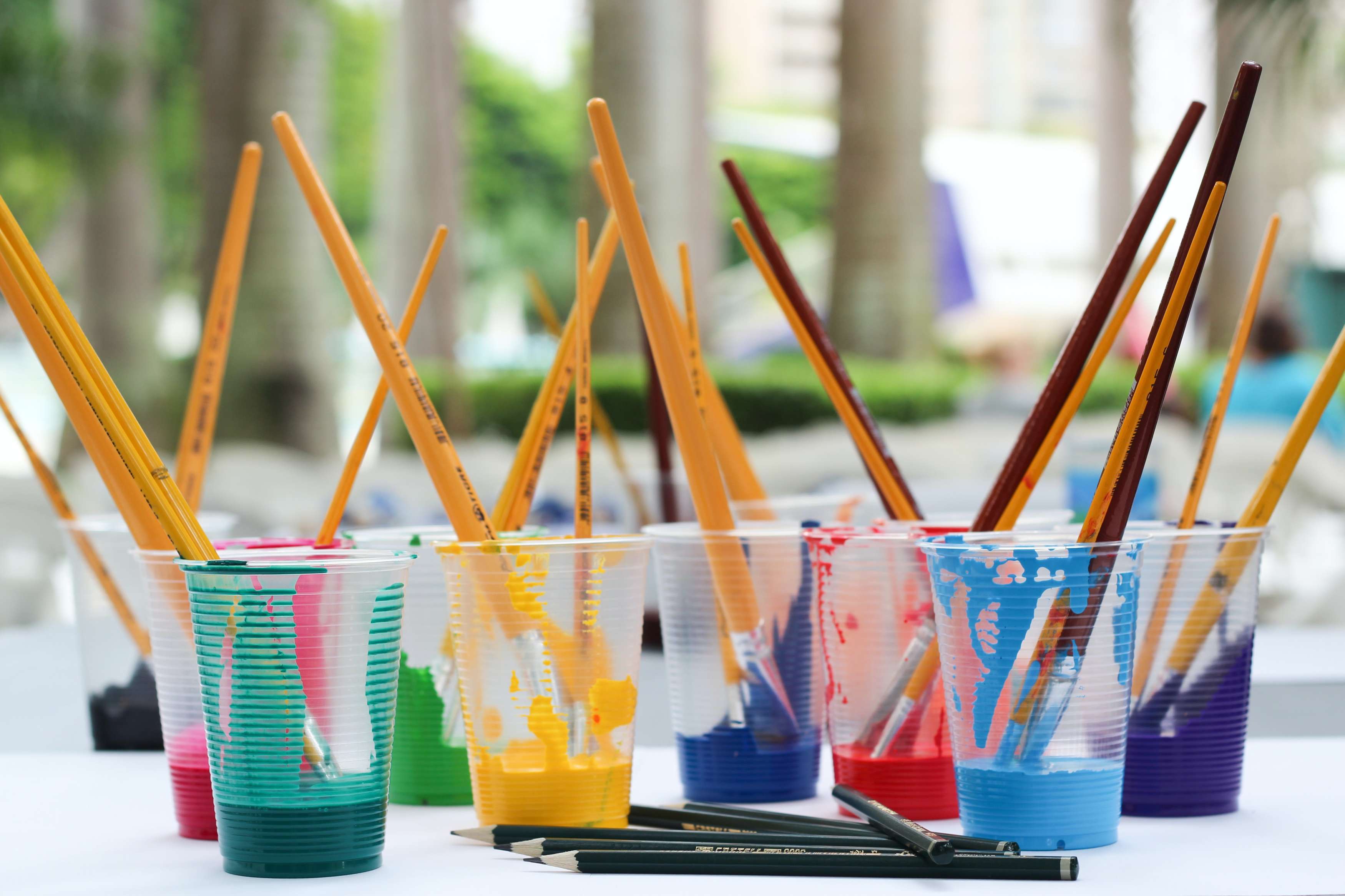 Cups filled with different colours of paint, each containing paintbrushes.